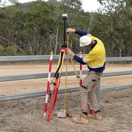Surveyor standing next to tripod using a tape measure to calculate the antenna height for the Emlid Reach RS2 base station